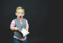 boy wearing gray vest and pink dress shirt holding book