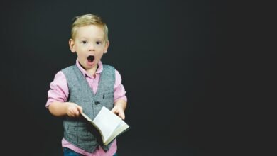 boy wearing gray vest and pink dress shirt holding book